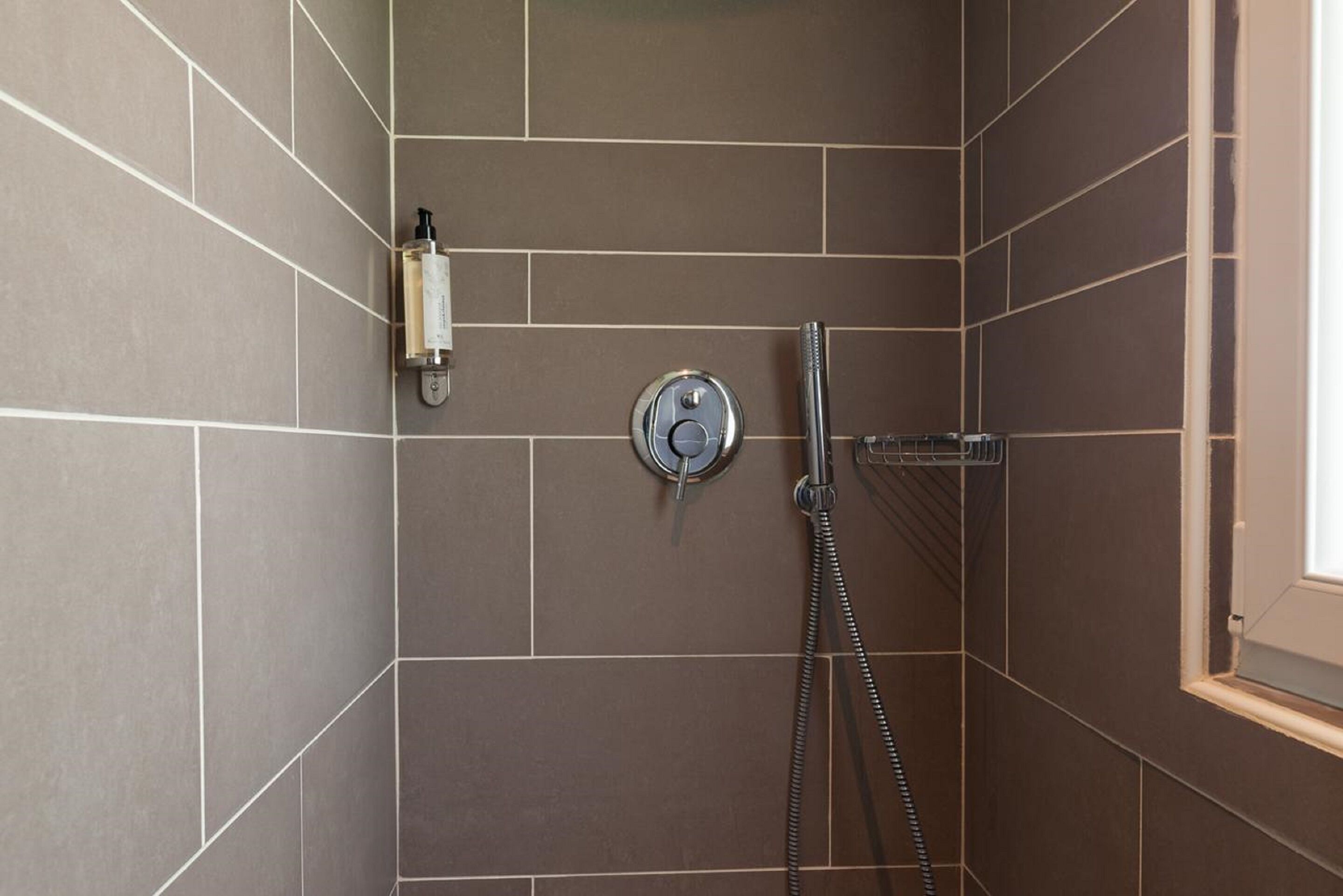Un área de ducha con ducha de mano y panel de control en la pared.