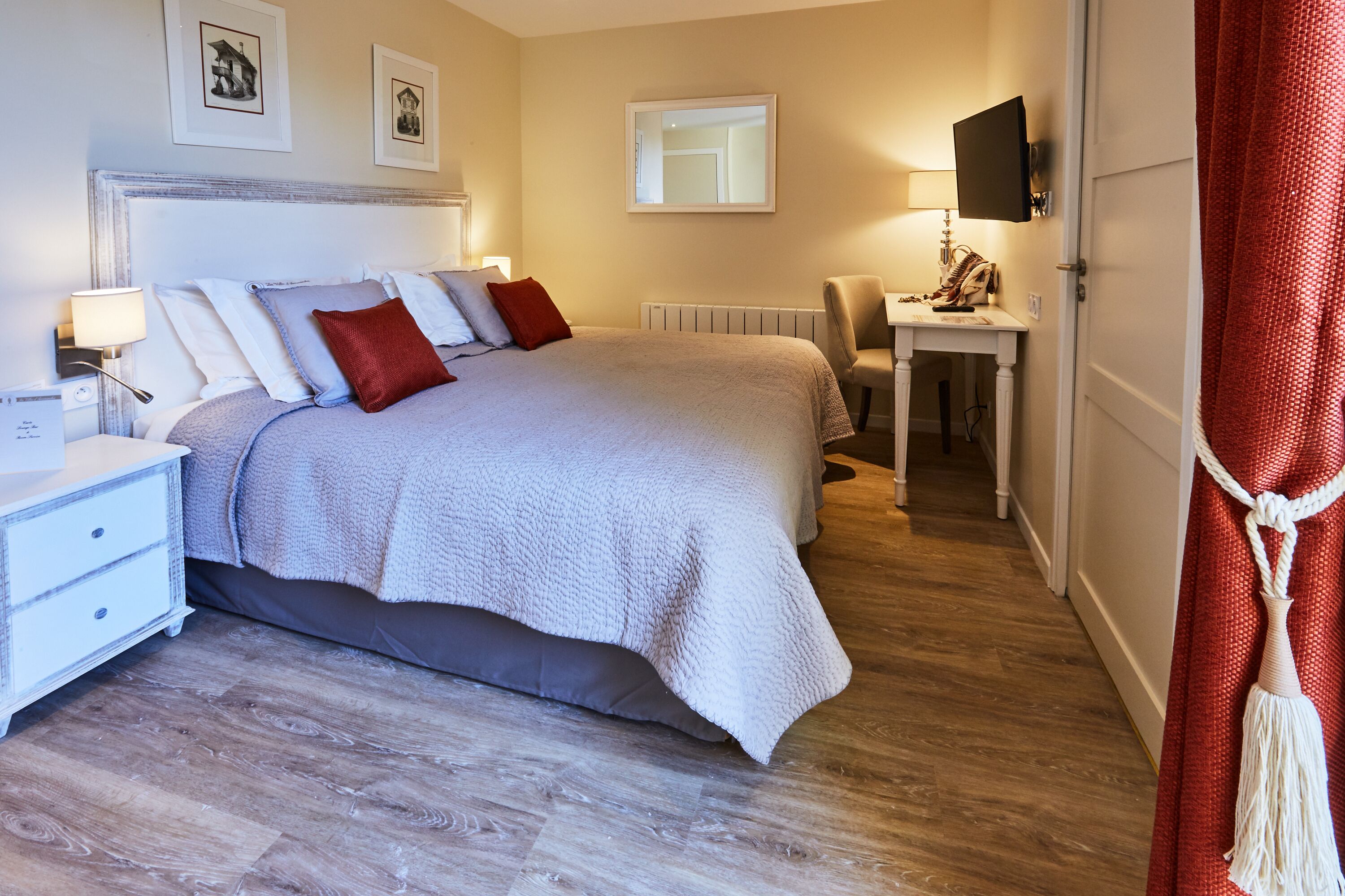 A neatly arranged bedroom with a bed, bedside table, lamp, and a desk with a chair.