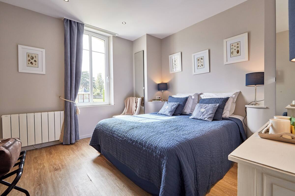 A bedroom with a large bed, a bedside table, a chair, a radiator, and a window with curtains.