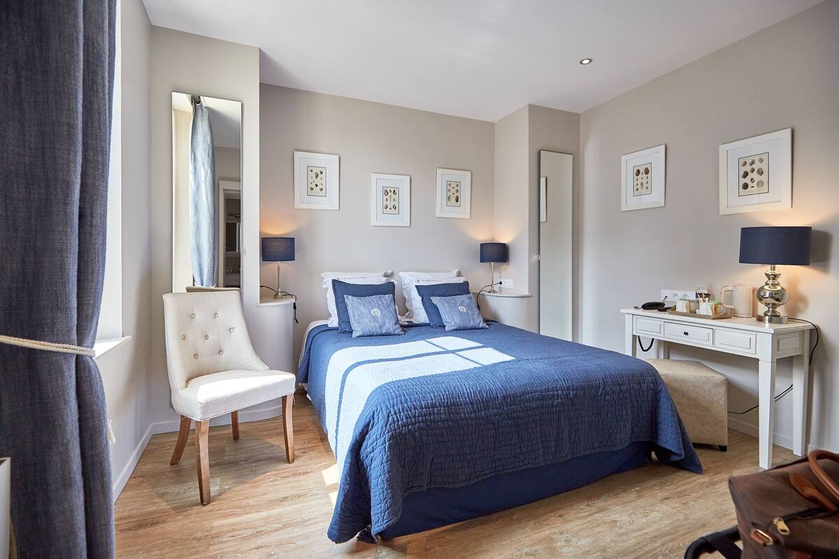 A bedroom with a bed, bedside tables, a desk, a chair, and artwork on the walls.