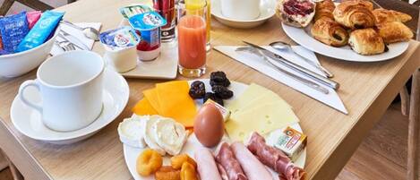 A breakfast table with various food items, including cheese, meats, fruits, and pastries.
