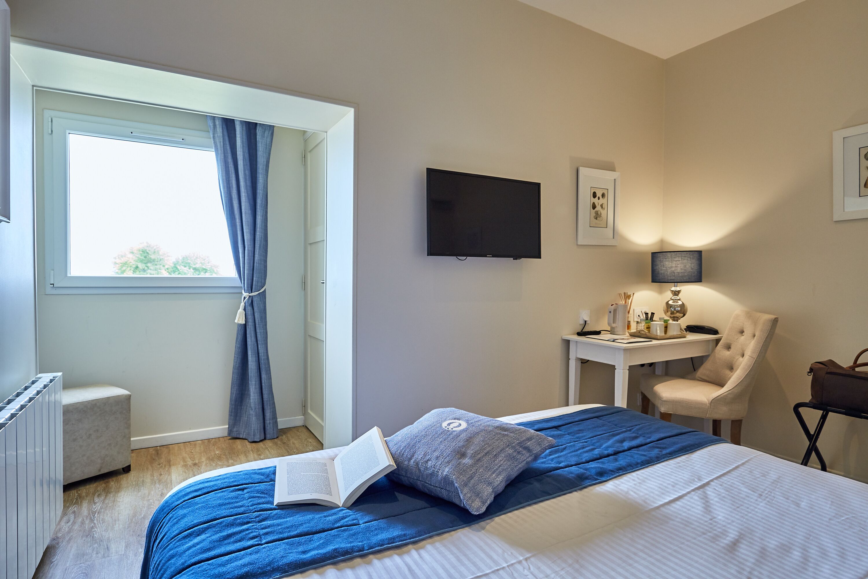 A bedroom with a bed, a desk, a chair, a TV, and a window with curtains.