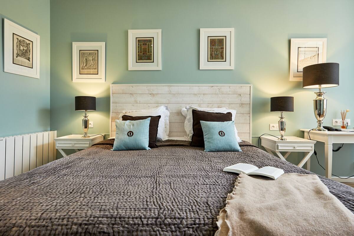 A neatly arranged bedroom with a large bed, two bedside tables, a nightstand, and framed pictures on the wall.