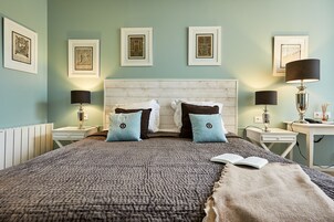 Un dormitorio ordenado con una cama grande, dos mesitas de noche y cuadros enmarcados en la pared.