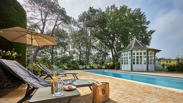A poolside area with lounge chairs, a table with a drink and snacks, and a gazebo.
