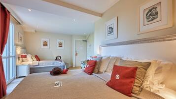 Een hotelkamer met een groot bed, een bureau en een stoel. Er hangen afbeeldingen in lijsten aan de muur en een raam met gordijnen.