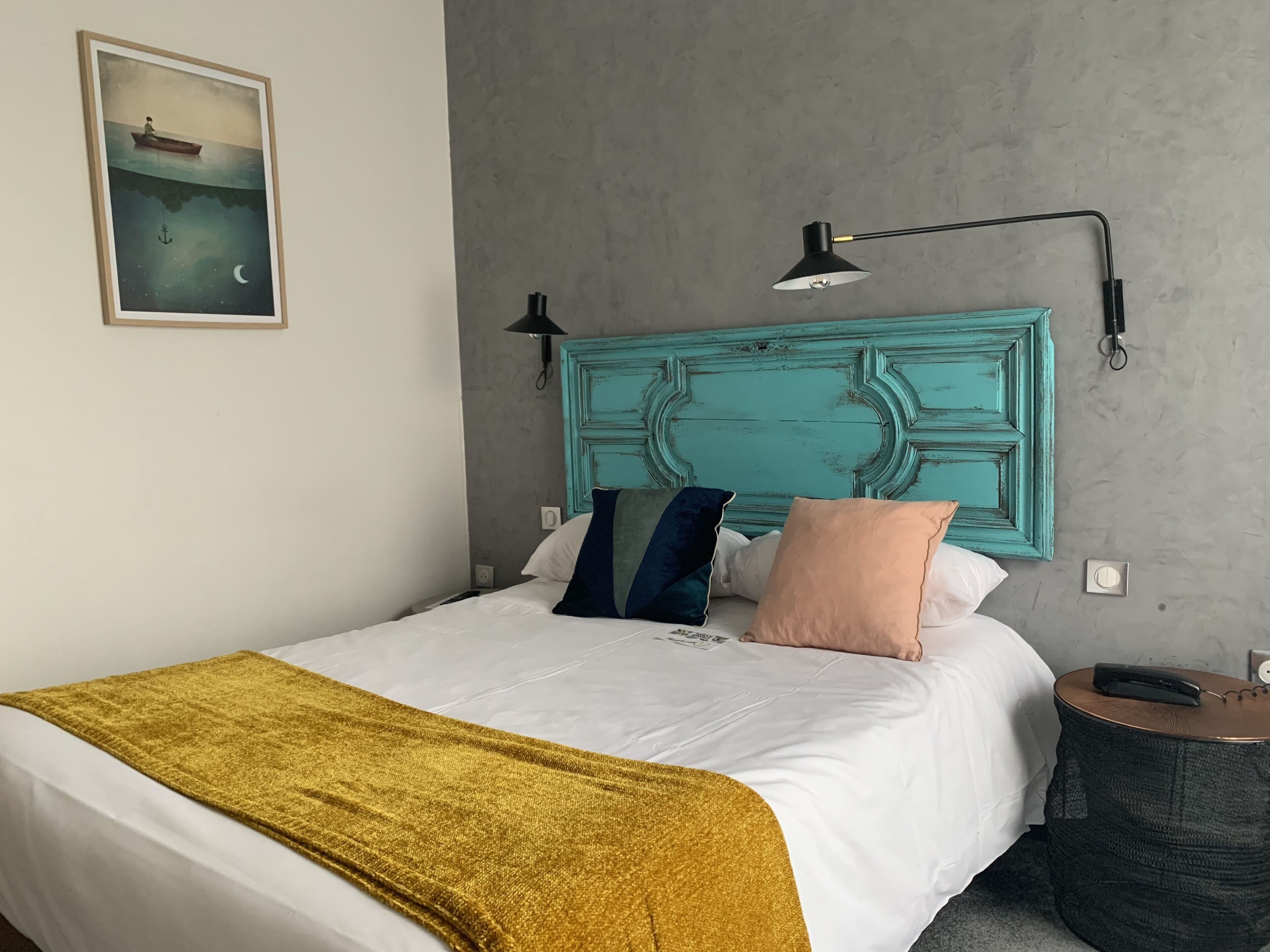 A neatly made bed with white and gold bedding, a teal headboard, and a single bedside lamp.