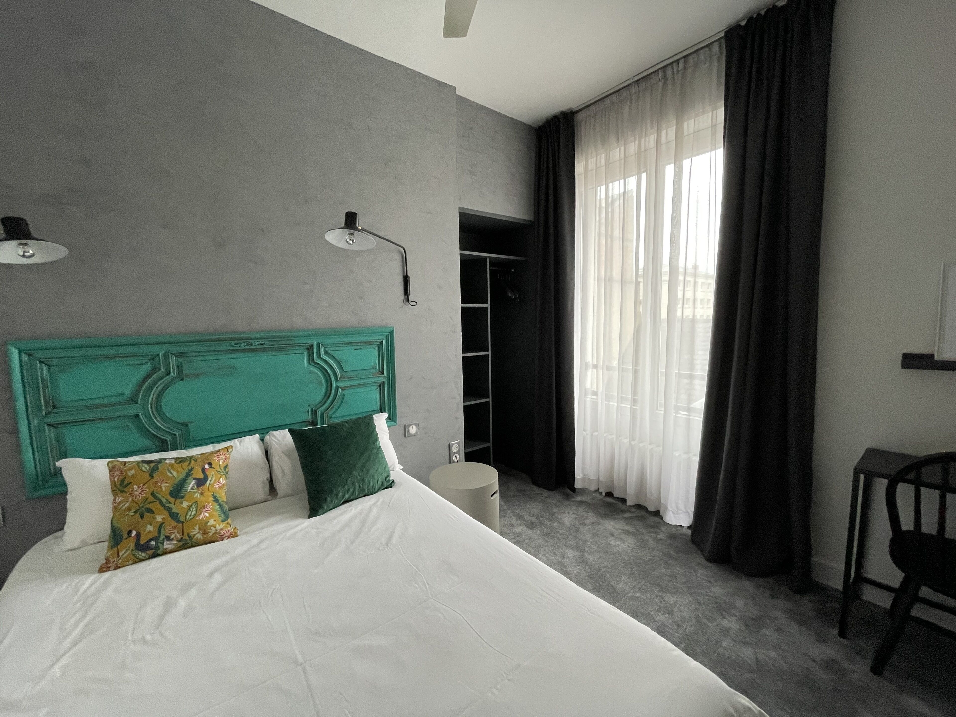 Ein modernes Hotelzimmer mit einem türkisblauen Kopfteil, einem großen Bett, einem Schreibtisch und einem begehbaren Kleiderschrank.