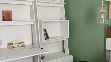 Ein Zimmer mit weißem Schreibtisch, Regalen, einem kleinen Hocker, einem Bett und einer grünen Wand.
