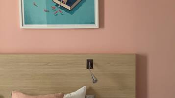 A bedroom with a bed, a bedside table, a pink toilet, and a framed artwork on the wall.