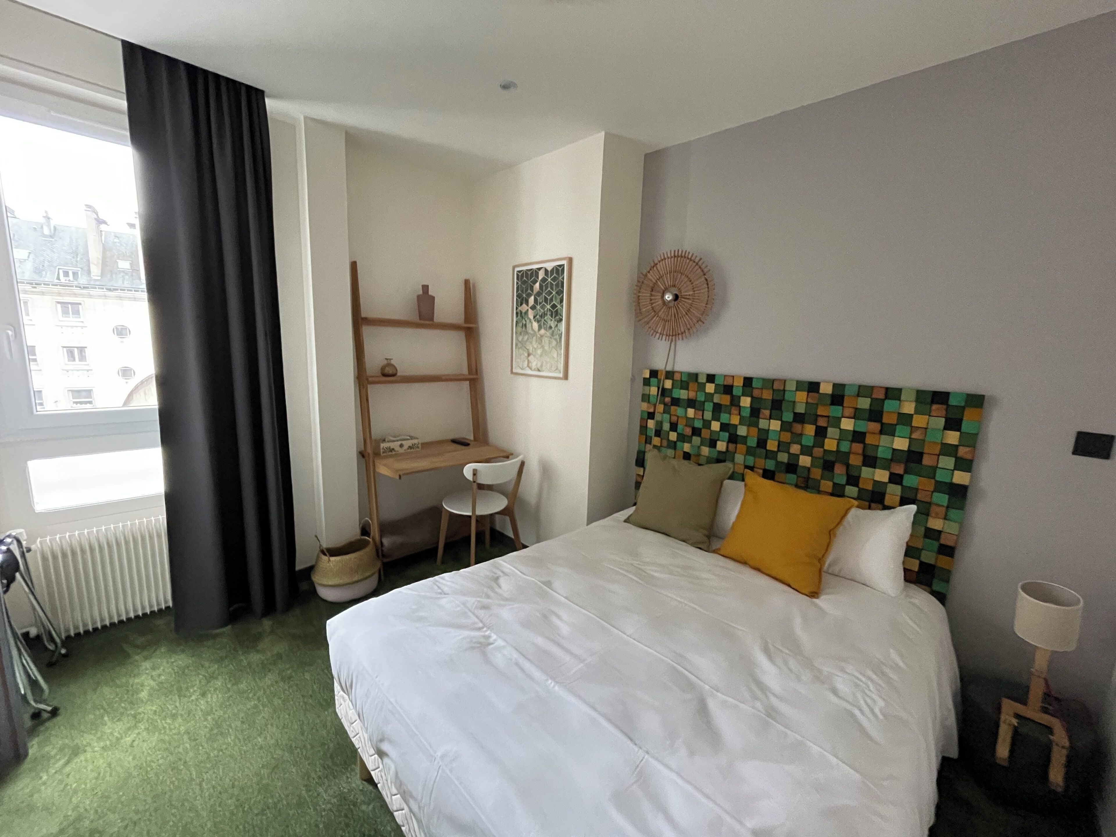 Hotelkamer met een bed, bureau, stoel, radiator en raam met gordijnen.