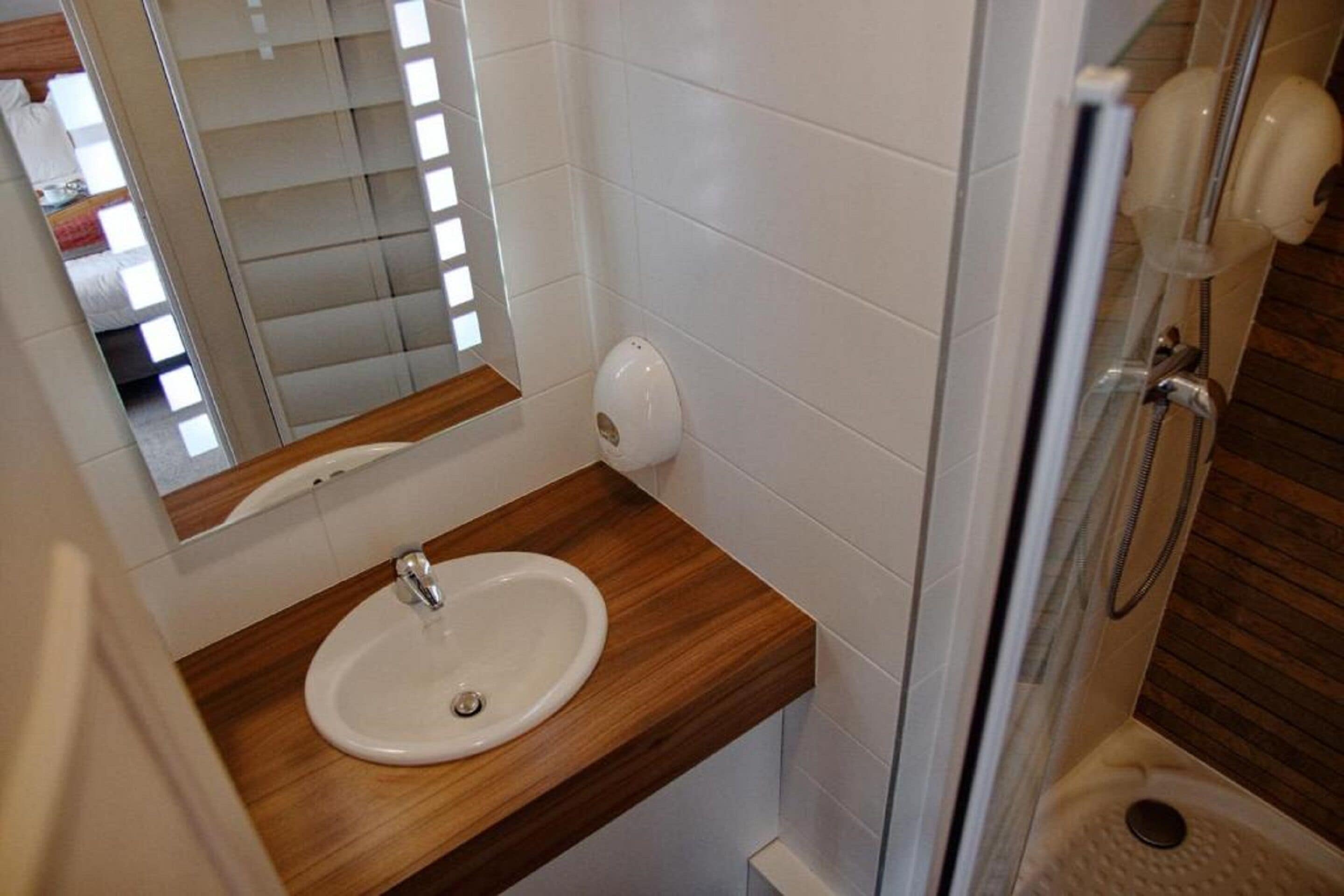 Une salle de bain avec un meuble-lavabo en bois, un lavabo blanc, un miroir et un espace douche.