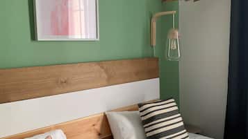 Une chambre avec deux lits, une tête de lit en bois, un luminaire fixé au mur, un tableau encadré et un portant à vêtements.