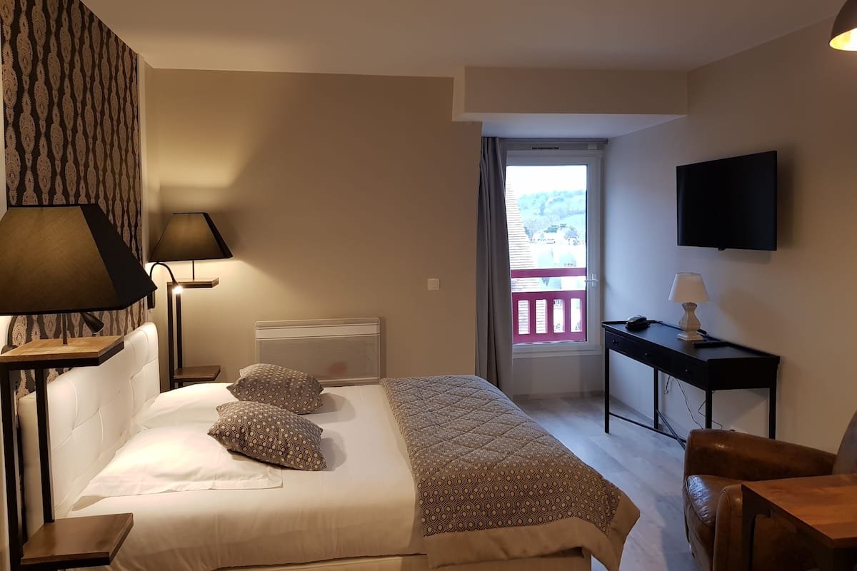 Una habitació d'hotel amb llit, làmpades de nit, escriptori, cadira i televisió.
