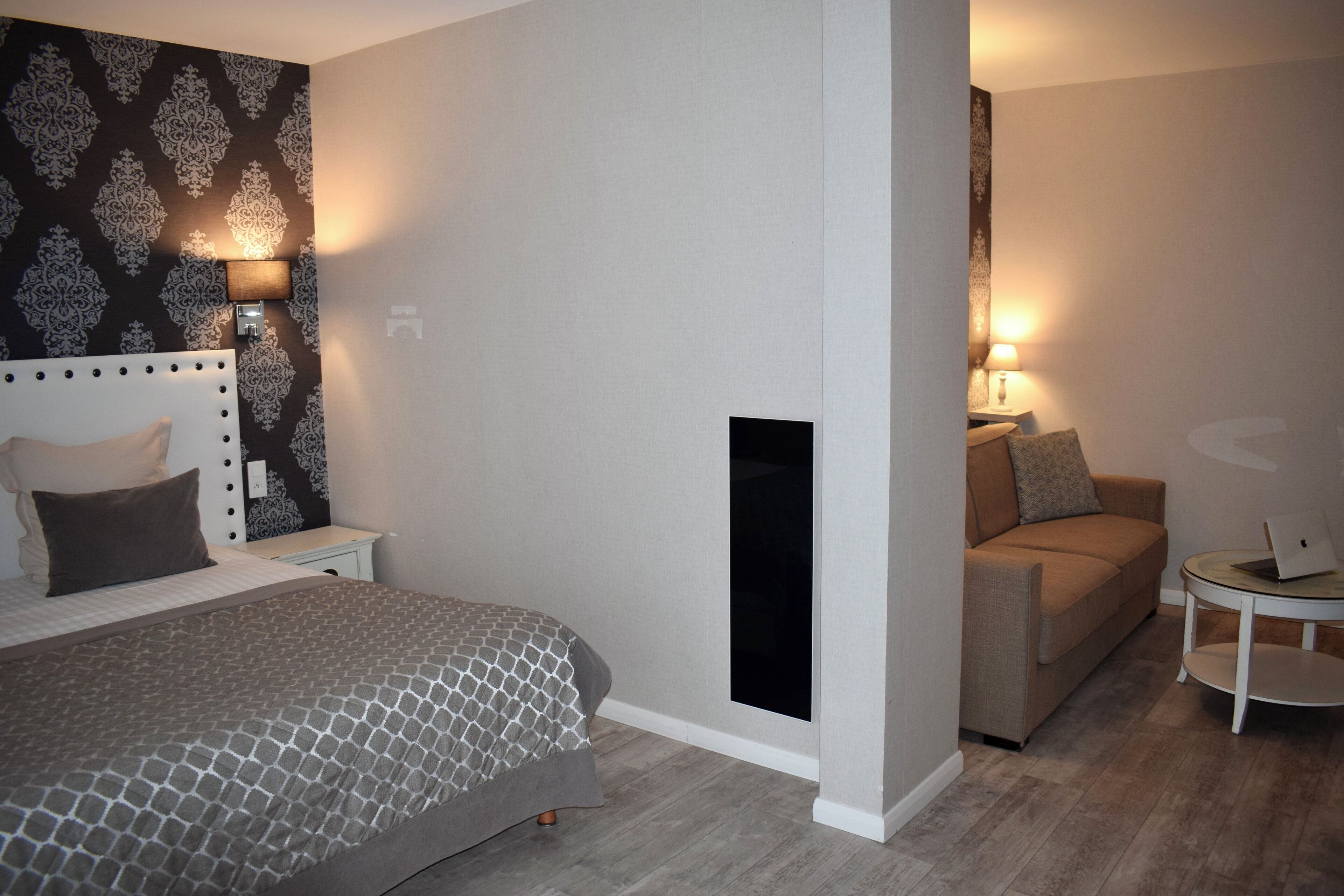 A hotel room with a bed, a sofa, a small table, and a wall-mounted TV.
