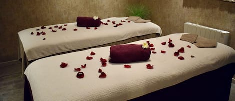 Two massage tables with towels and rose petals, a potted plant, and a radiator.