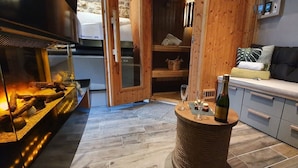 Une pièce chaleureuse avec une cheminée, un banc en bois, une petite table avec une bouteille et des verres, et un canapé avec des coussins.