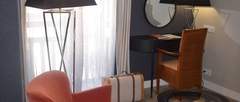 Una habitación con una silla moderna, una mesita, una lámpara de pie, una maleta y un escritorio con un espejo.