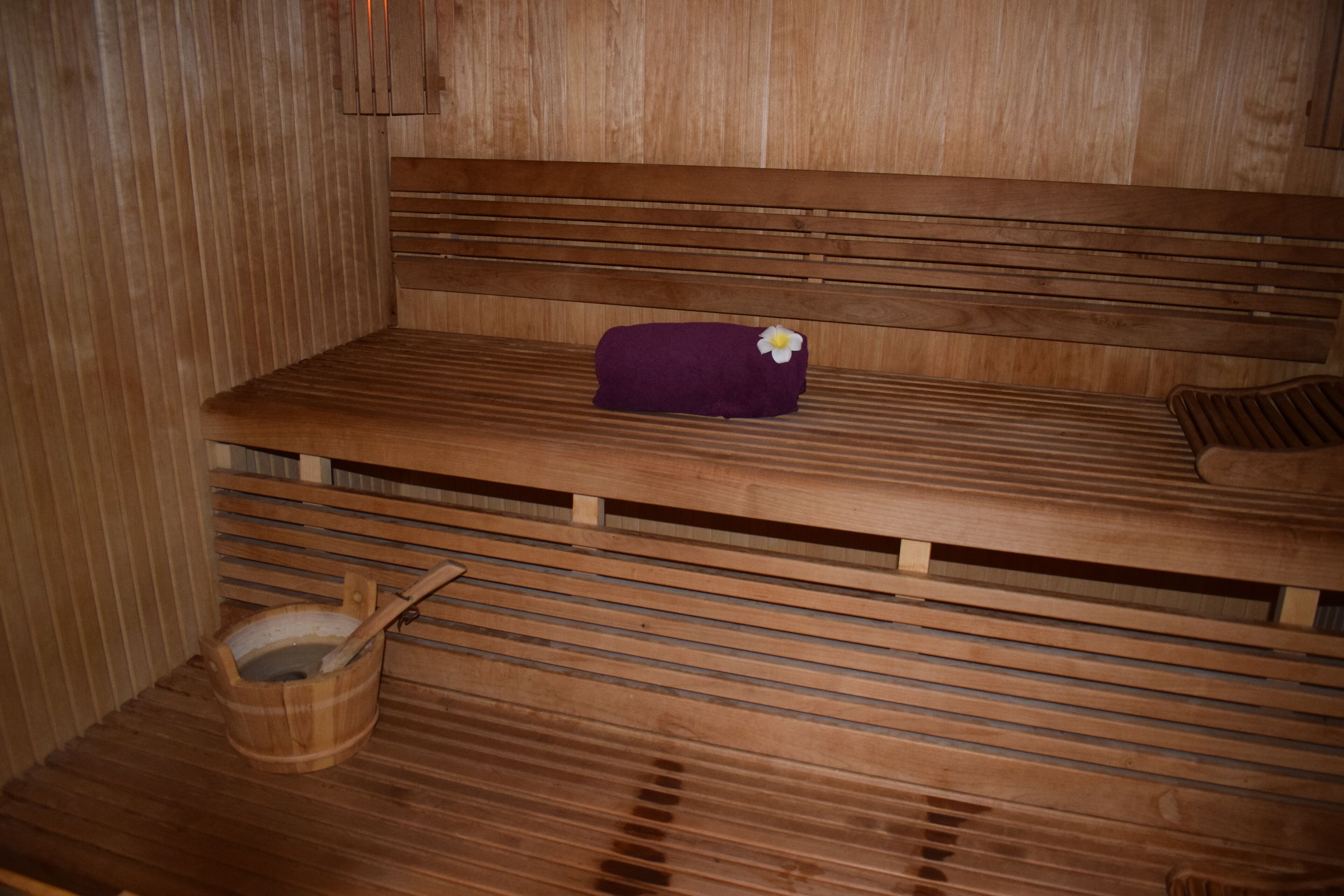 A wooden sauna bench with a towel and a flower.
