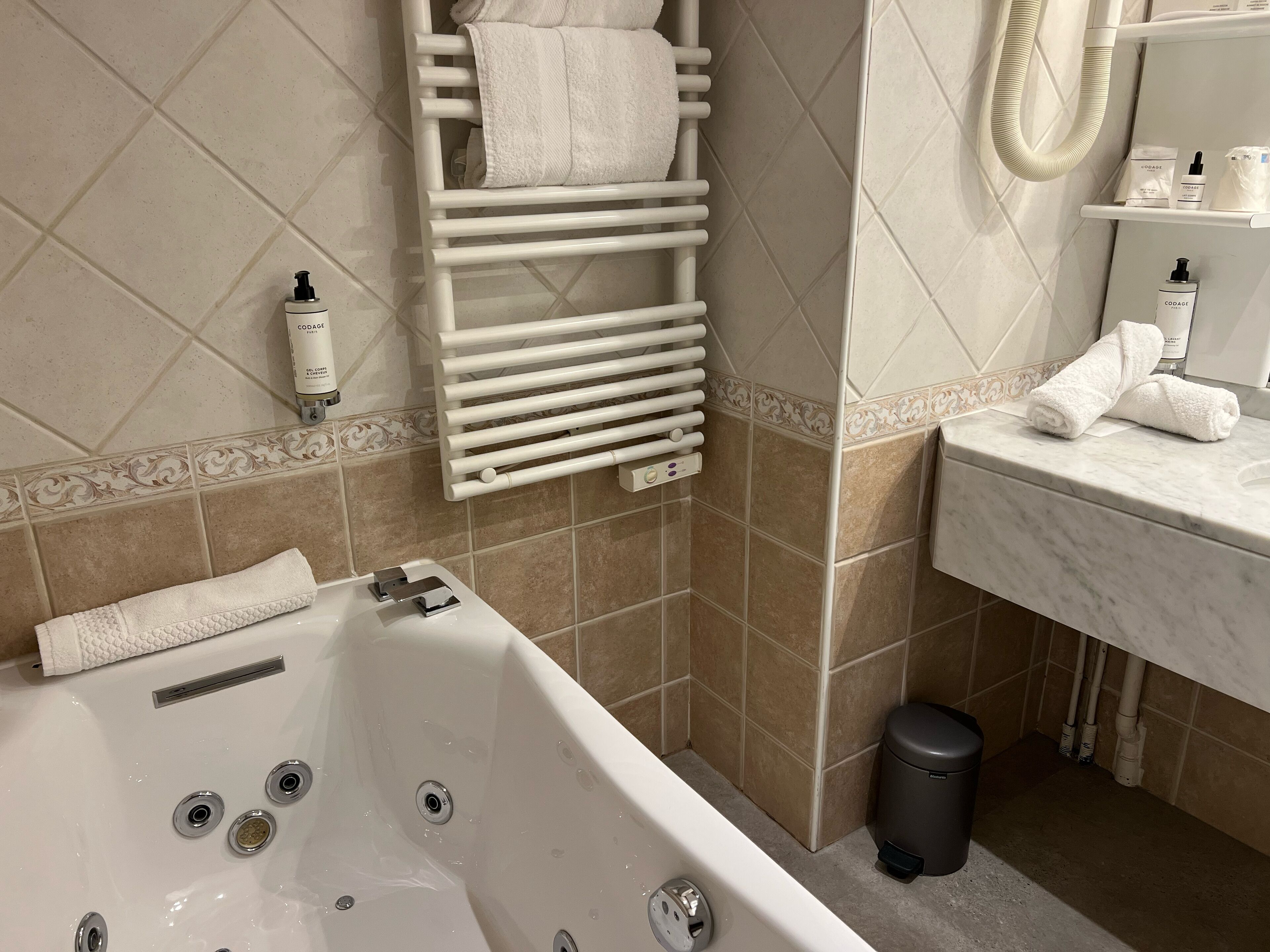 A bathroom with a bathtub, a towel rack, a sink, and toiletries.