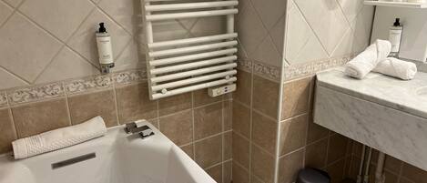 A bathroom with a bathtub, a towel rack, a sink, and toiletries.