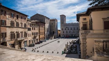 A historic square with stone buildings, a central tower, and a paved area with bollards.