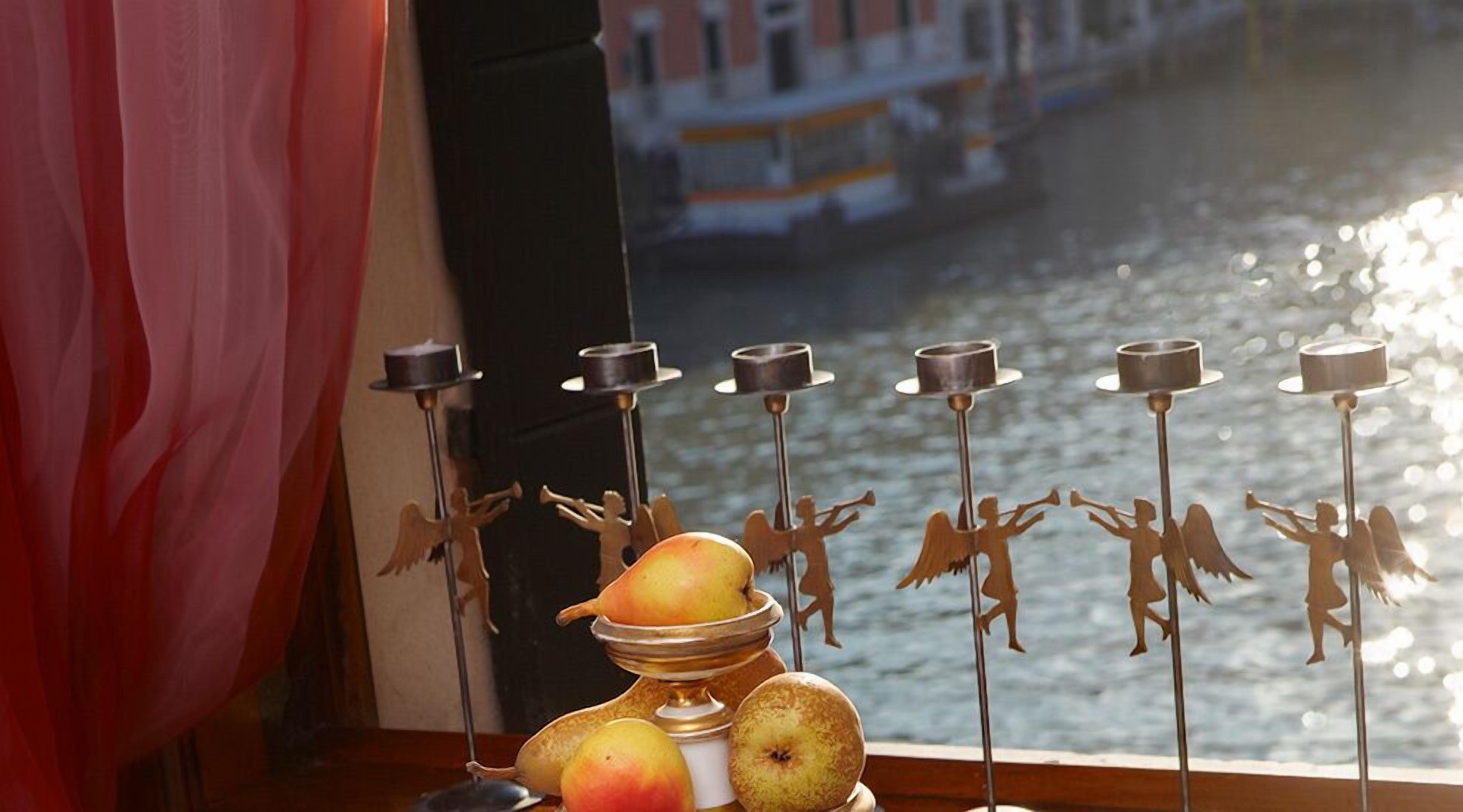 A table with fruit and candles by a window overlooking a canal.