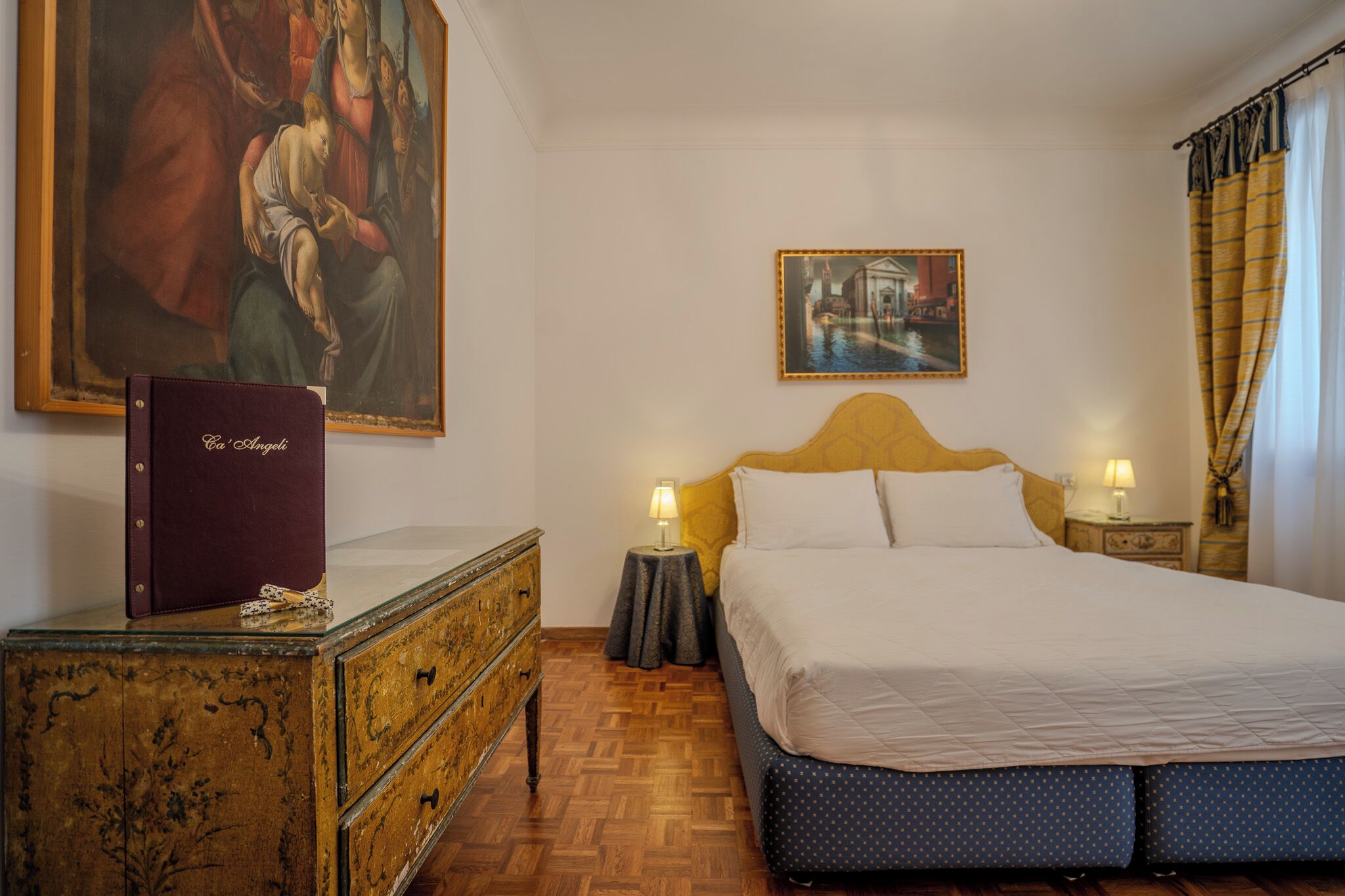 Un dormitorio con una cama, un tocador, una mesita de noche, una lámpara y dos cuadros en la pared.