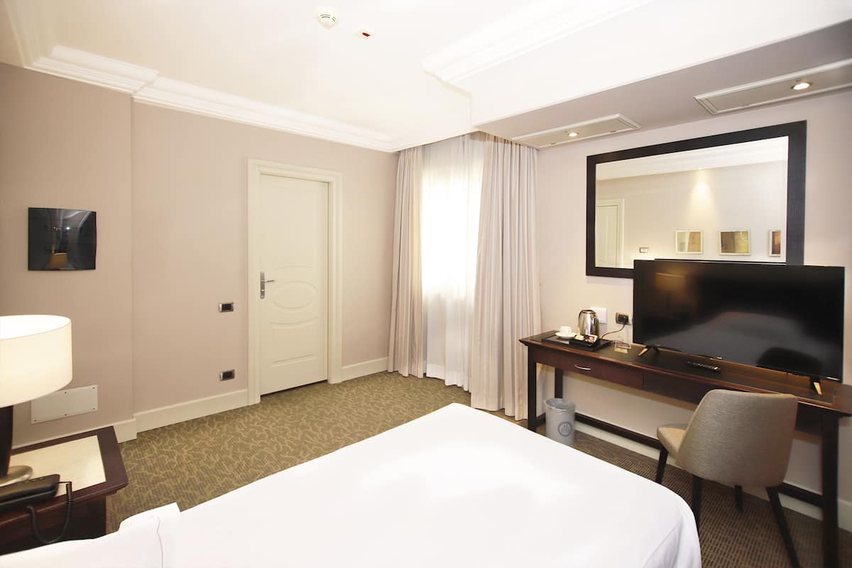 Een hotelkamer met een bed, een bureau met een televisie, een stoel, een lamp en een deur.