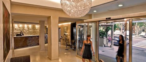 A hotel lobby with a reception desk, a large chandelier, and a glass door entrance.