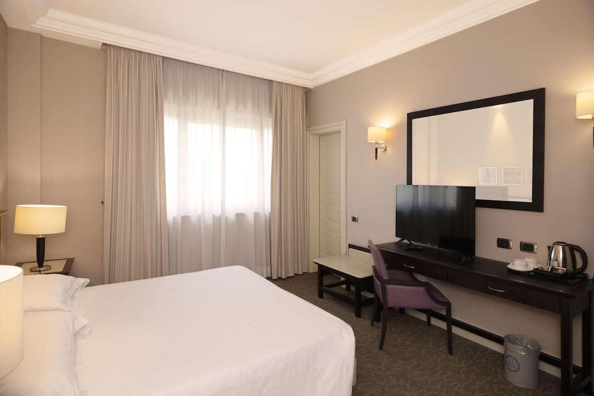 Een hotelkamer met een groot bed, een bureau met stoel, een televisie en een spiegel.