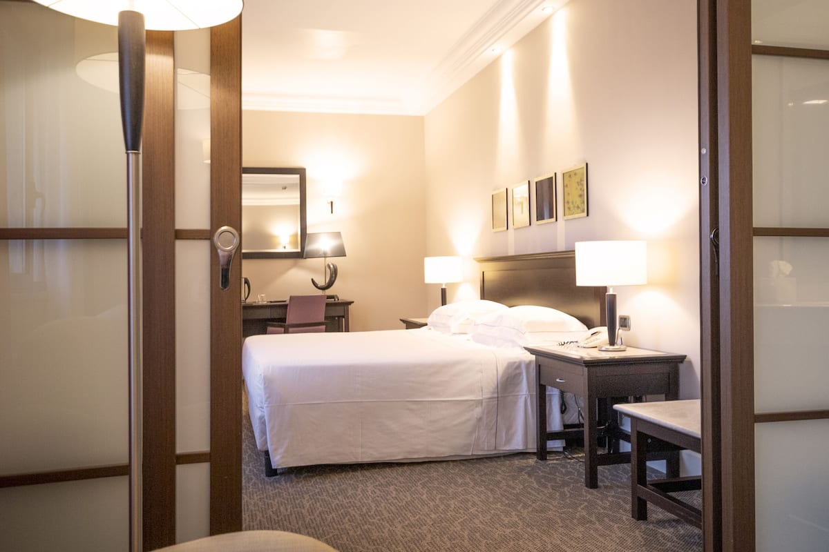 Een hotelkamer met een bed, twee nachtkastjes, een stoel, een bureau en een lamp.