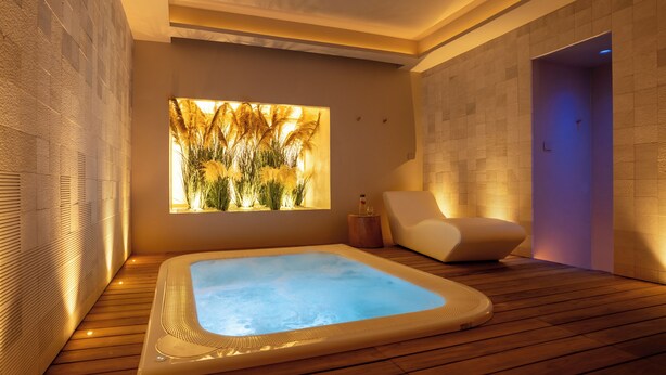 Un moderno cuarto de spa con hidromasaje, piso de madera, una silla cómoda y una ventana con vistas a pastizales.