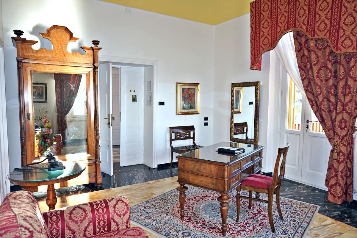 Una habitación con un escritorio de madera, una silla, un sofá, un espejo grande y una alfombra estampada.