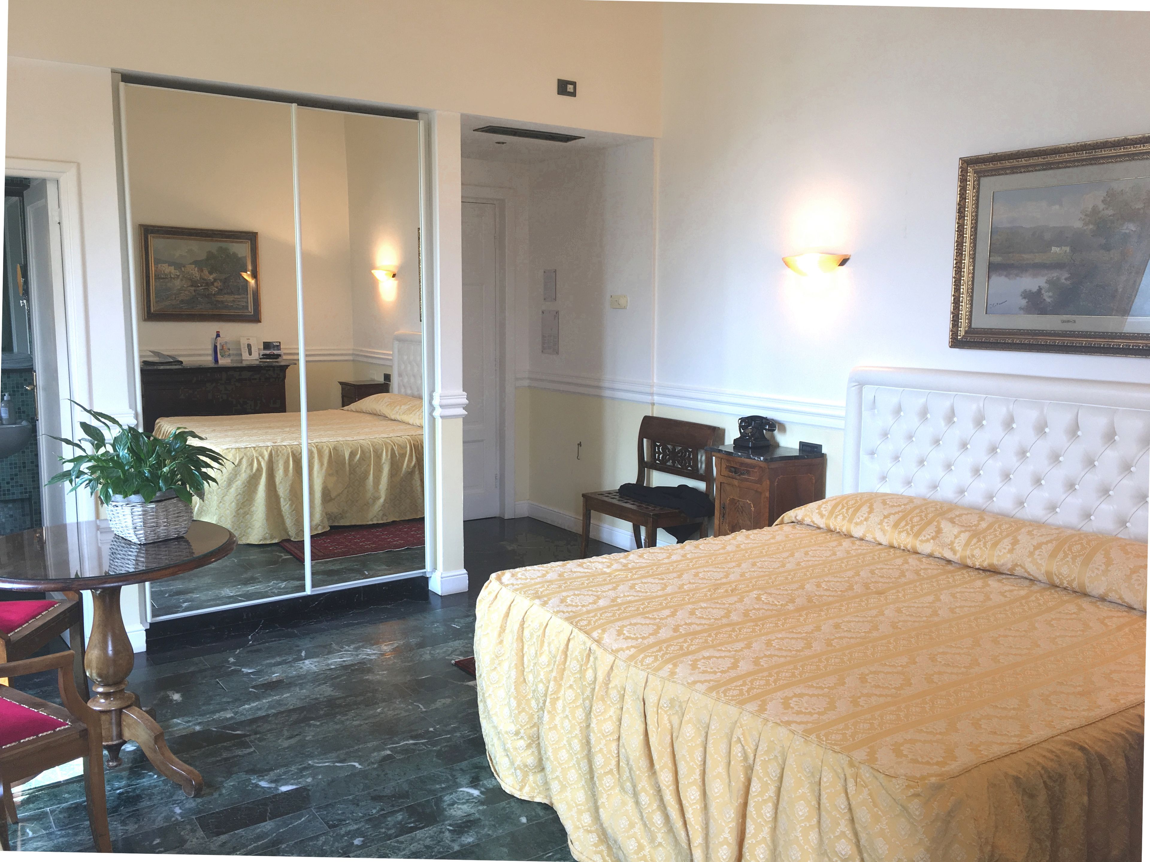 Ein Hotelzimmer mit einem Bett, einem Sessel, einem Tisch mit Pflanze, einem Spiegel und einem Bild an der Wand.