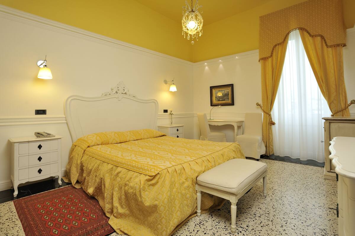 Un dormitorio con cama, mesita de noche, lámpara y una alfombra roja estampada.