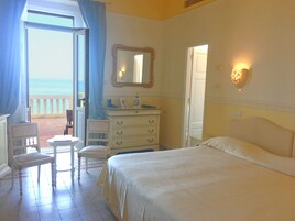 Una camera da letto con un letto, una cassettiera, una sedia e una scrivania. Si vede l'oceano dalla finestra.