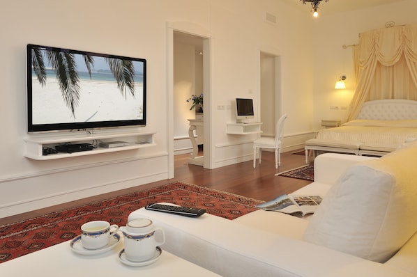 Una habitación de hotel moderna con televisión de pantalla plana, un sofá cómodo, una mesita de noche con lámpara y una cama con cortinas.