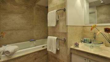 Un bagno con una vasca, due asciugamani su porta-asciugamani, un lavandino in vetro con un vaso di fiori e uno specchio sopra il lavandino.