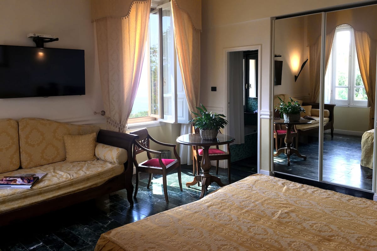 Habitación de hotel con sofá, cama, mesa de comedor con sillas, televisor montado en la pared y un espejo grande.