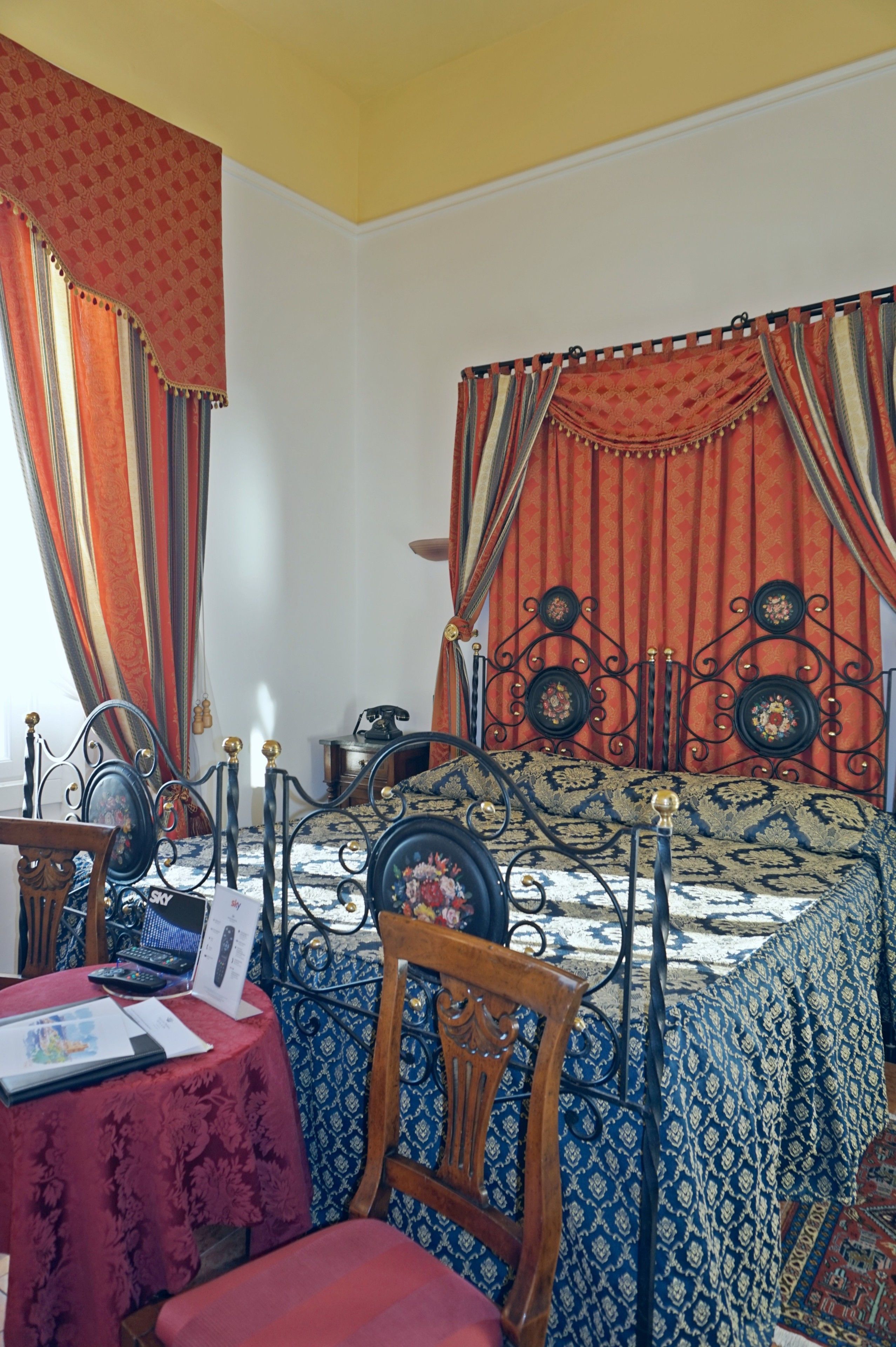 A room with a bed, a wooden chair, a table with a red tablecloth, and curtains.