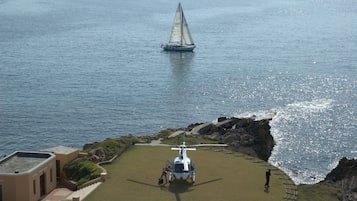 A helicopter on a helipad near a coastal area with a sailboat in the water.