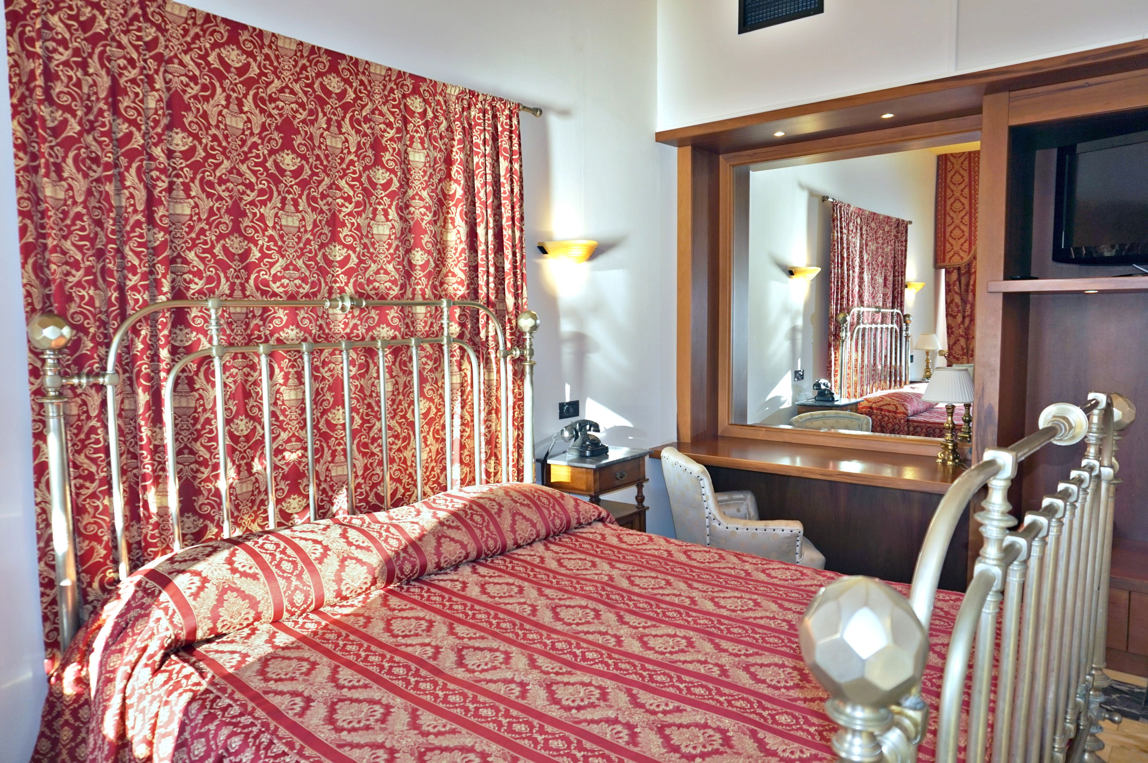 A hotel room with a bed, a desk, a chair, a mirror, and a television.