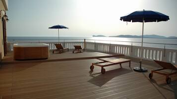 A wooden deck with lounge chairs and a hot tub, overlooking the sea.