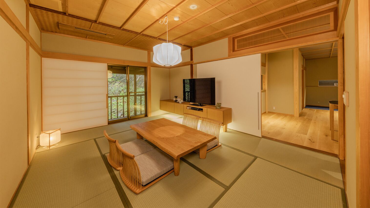 A traditional Japanese room with tatami flooring, a low wooden table, a television, and sliding doors.
