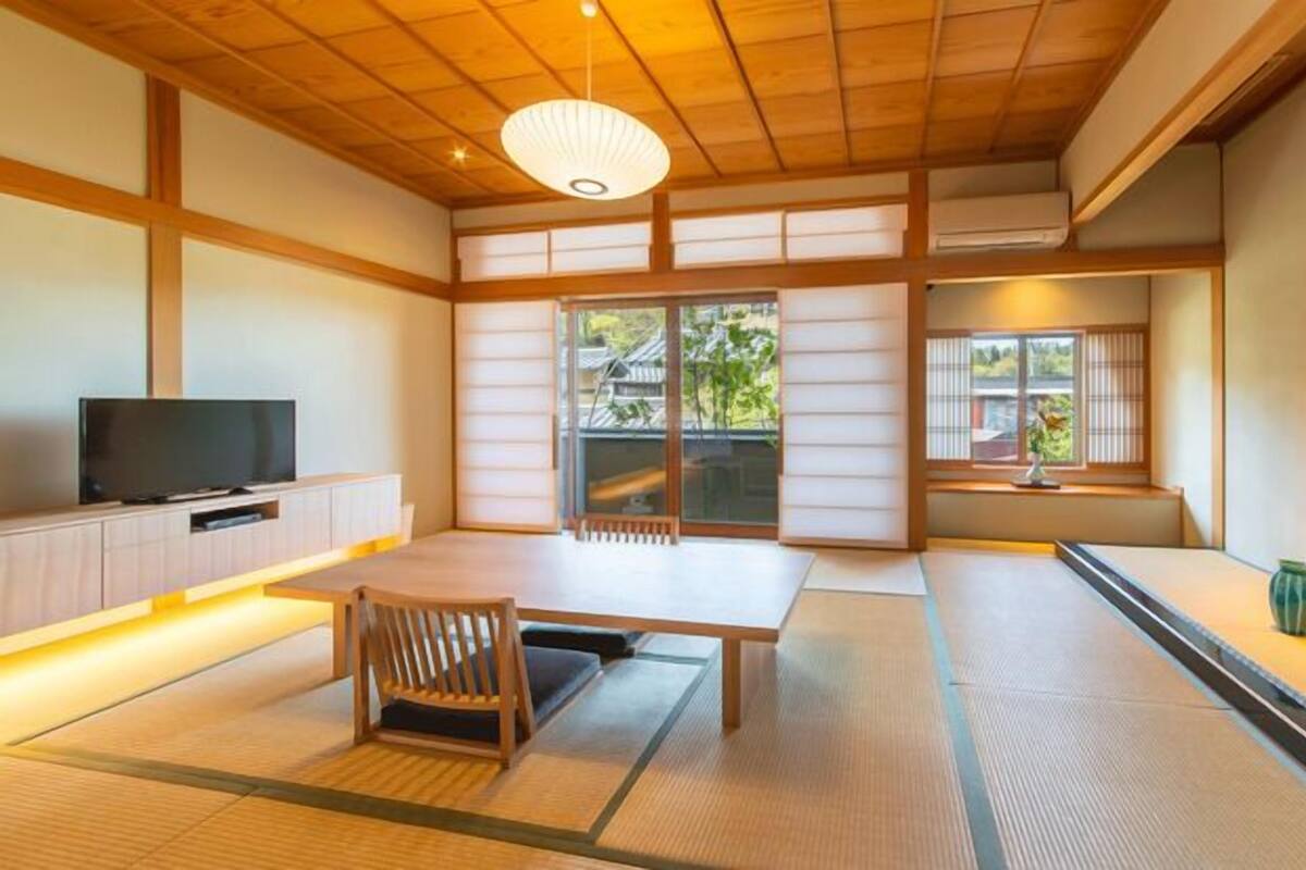 A traditional Japanese room with tatami flooring, a television, sliding doors, and a wooden ceiling.