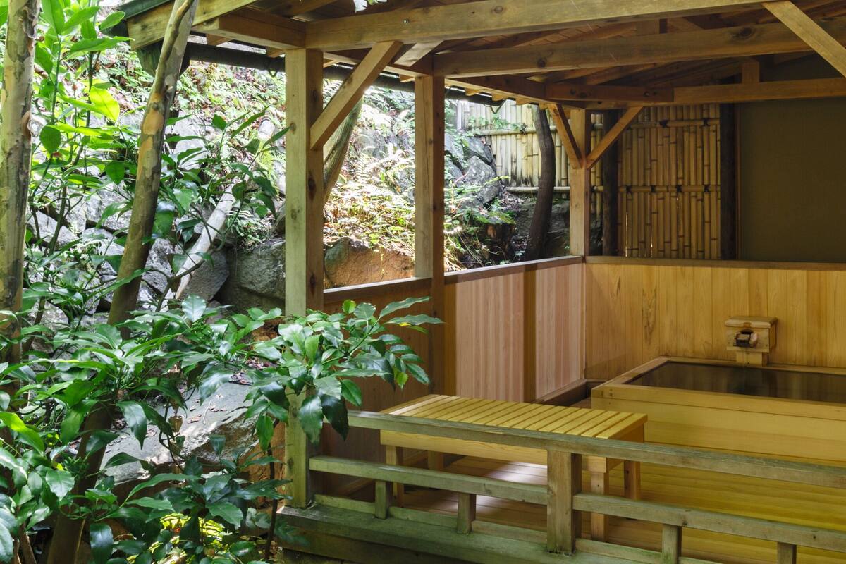 A traditional wooden bathhouse with a wooden bench and a stone wall in the background.