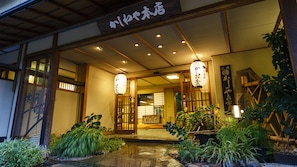 Un edificio japonés tradicional con entrada de madera, faroles y plantas en macetas.