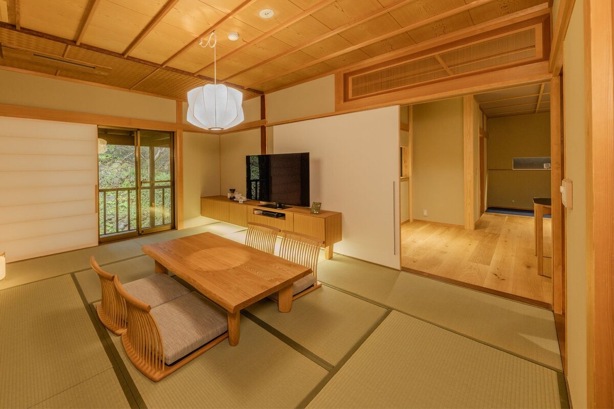 Ett traditionellt japanskt rum med tatamimattor på golvet, ett lågt träbord, en tv och skjutdörrar.