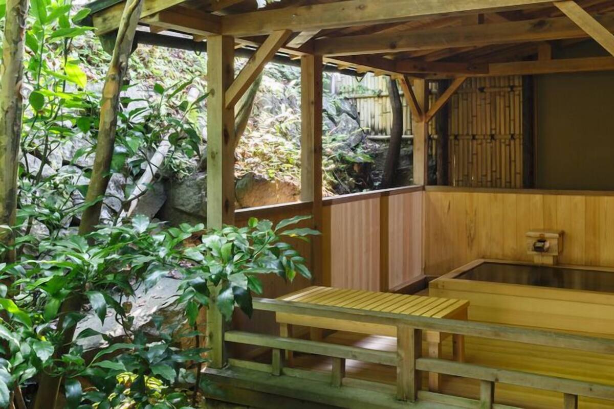 A wooden hot spring bath area with a wooden bench and a stone wall in the background.